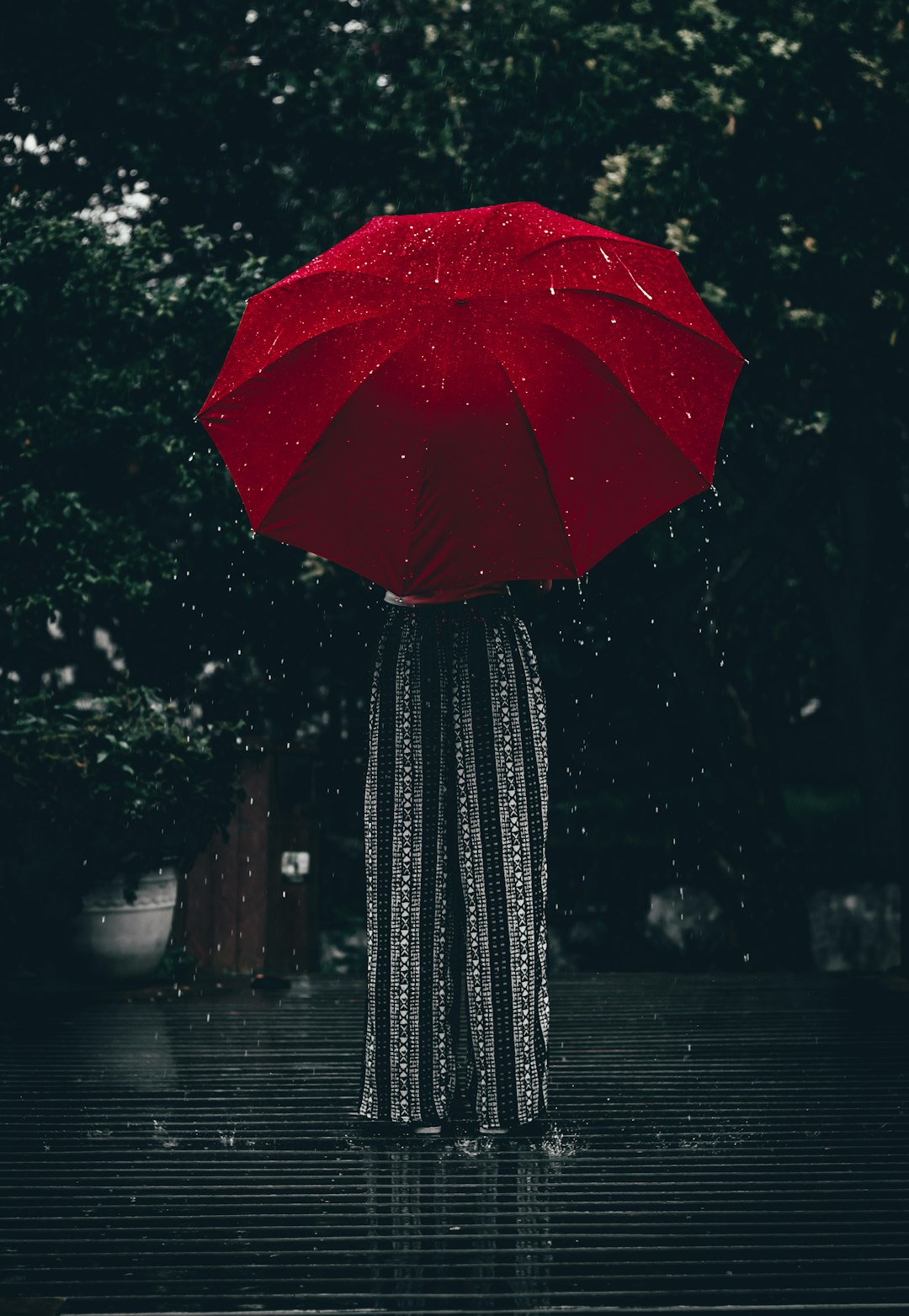 woman in patterned pants holding a red umbrella in front of her top half