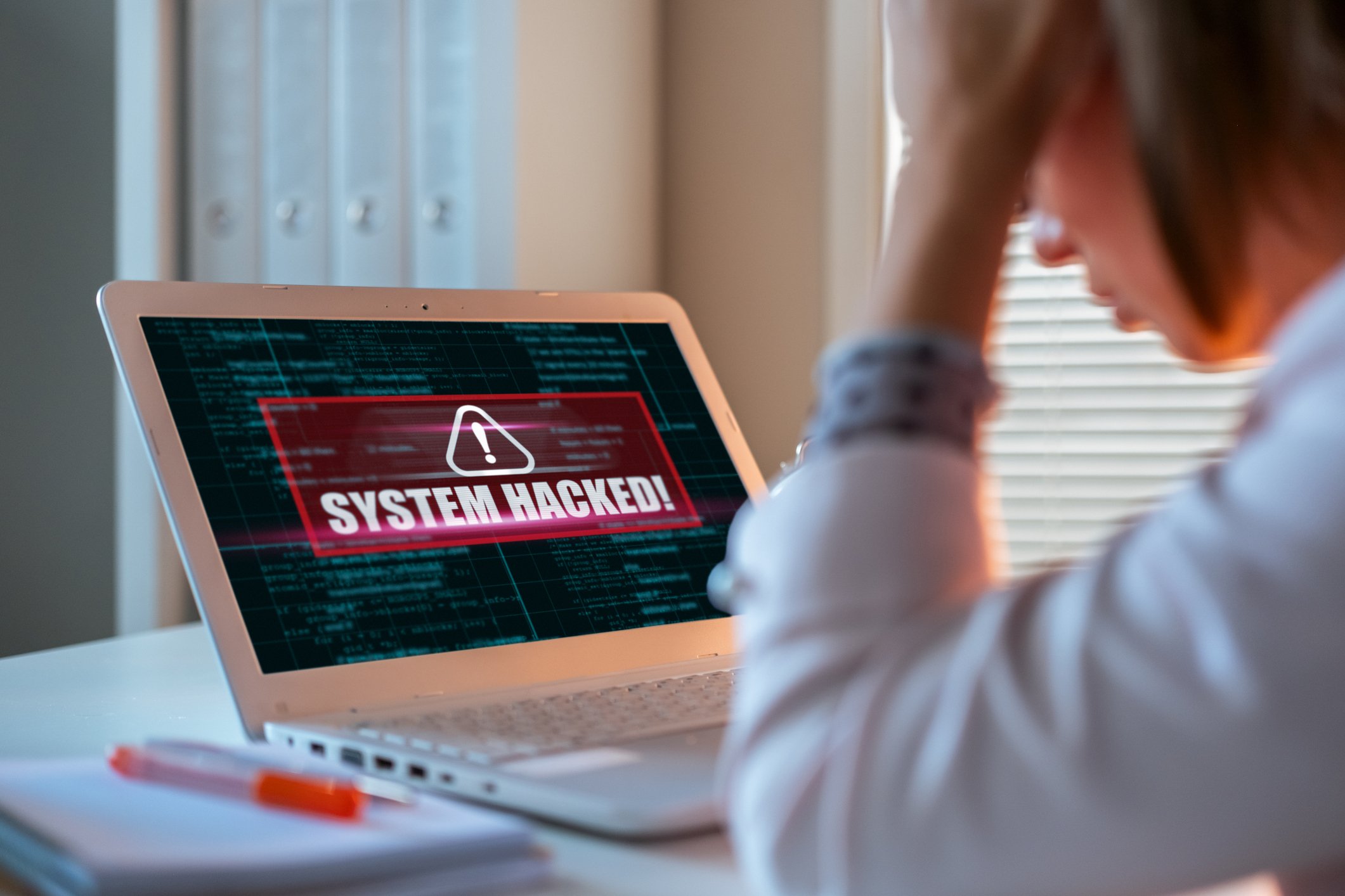 laptop screen with the words system hacked on the screen and person with head in their hand