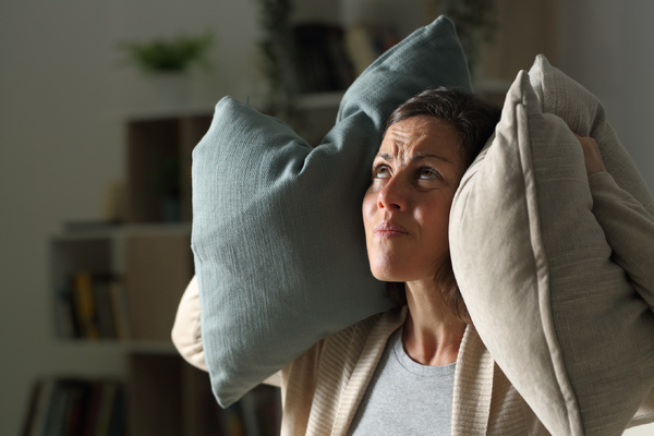 distressed woman looking upward holding pillows over both ears