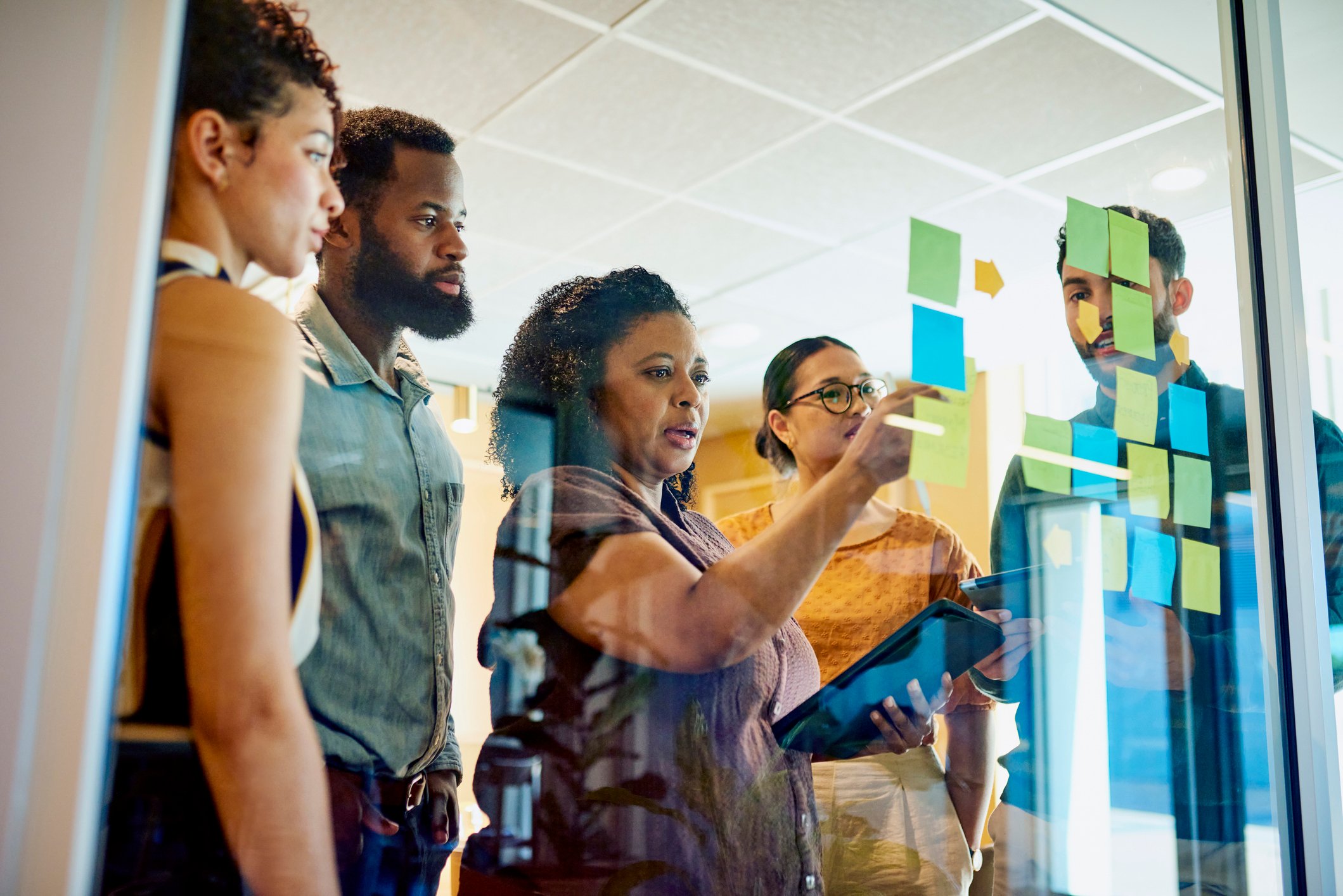 five professionals discussing sticky notes on window