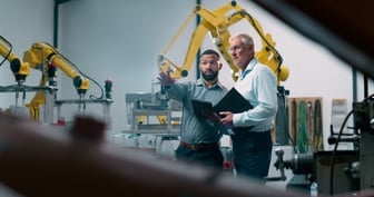 two men in collared shirts talking at a manufacturing facility